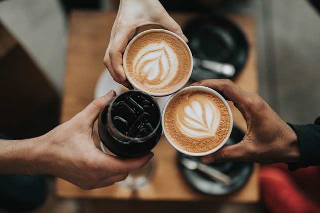 Three people clinking their coffee mugs together at an independent coffee shop