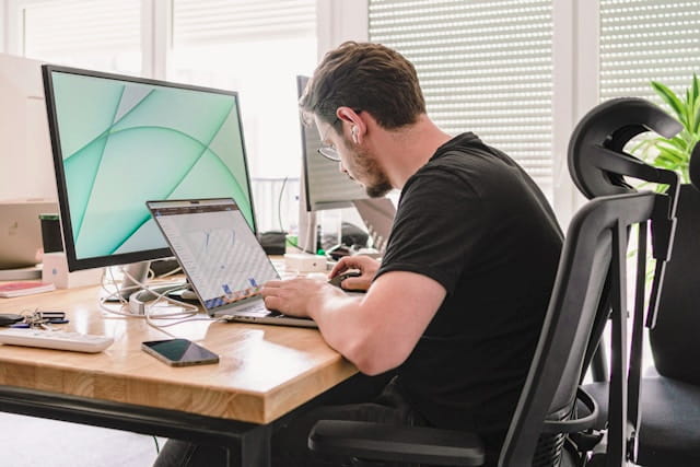 Digital marketing specialist working across a desktop monitor and laptop.