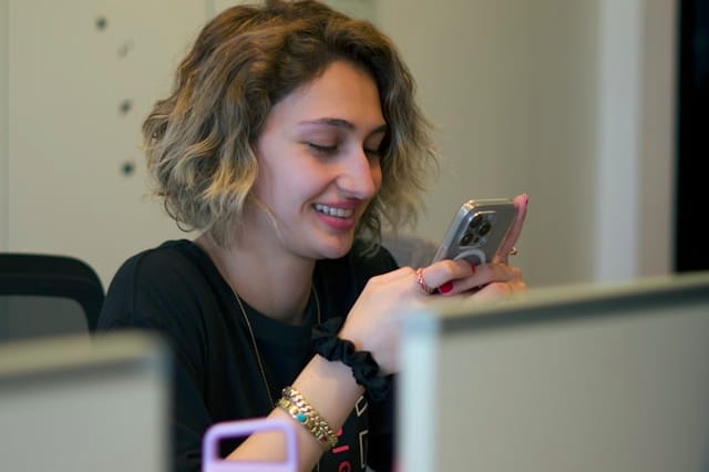 Woman smiling while using a smartphone at her office desk.
