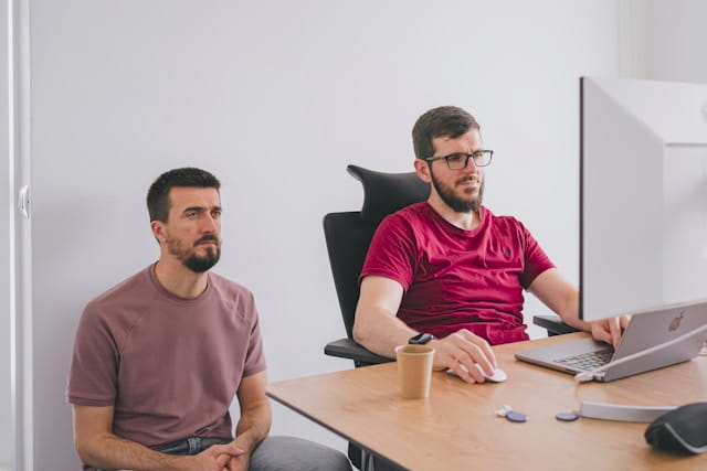Two web developers reviewing work together on a large computer screen.
